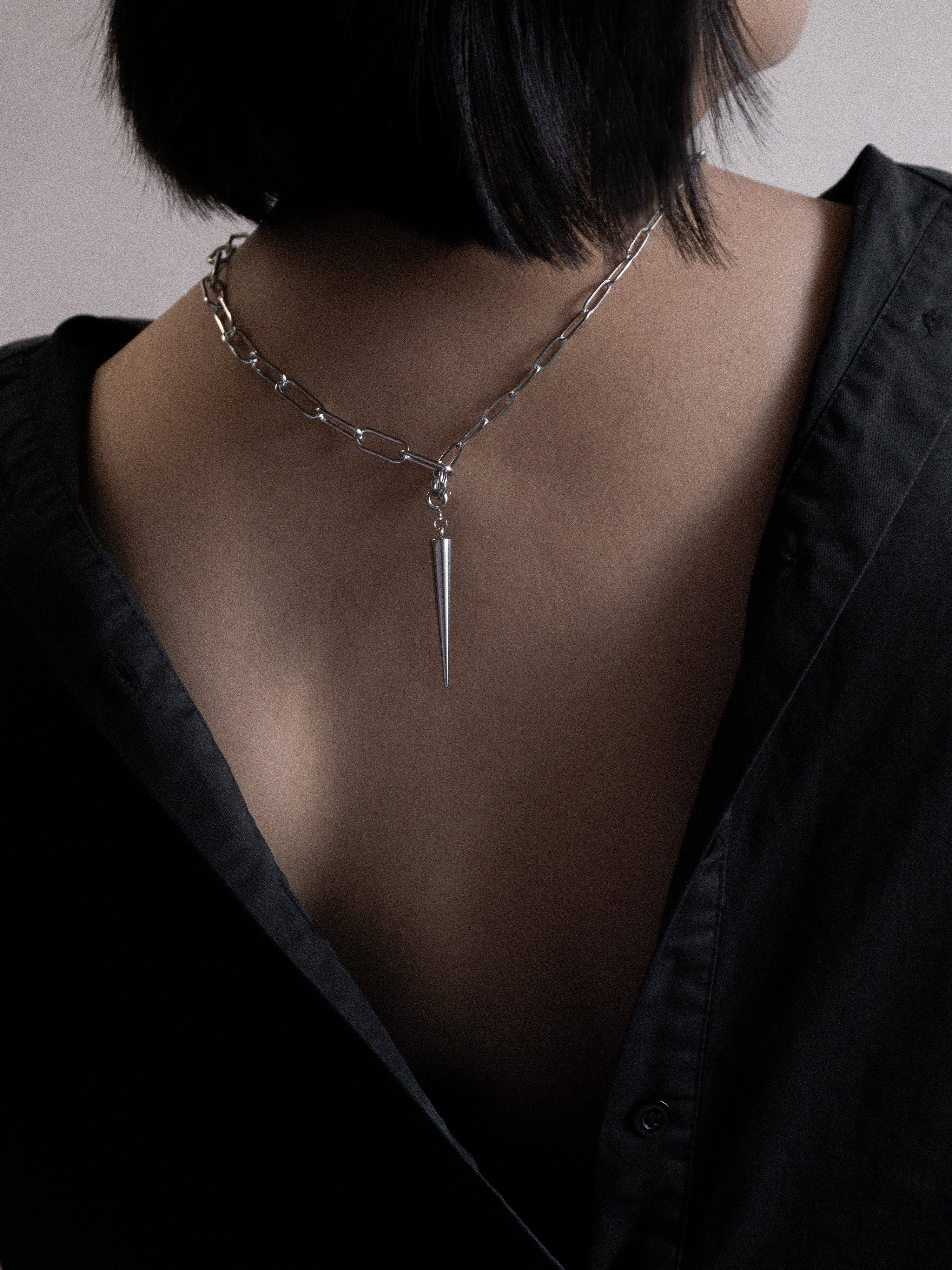 Person wearing a unique necklace on the back with a sharp pendant on a plain background