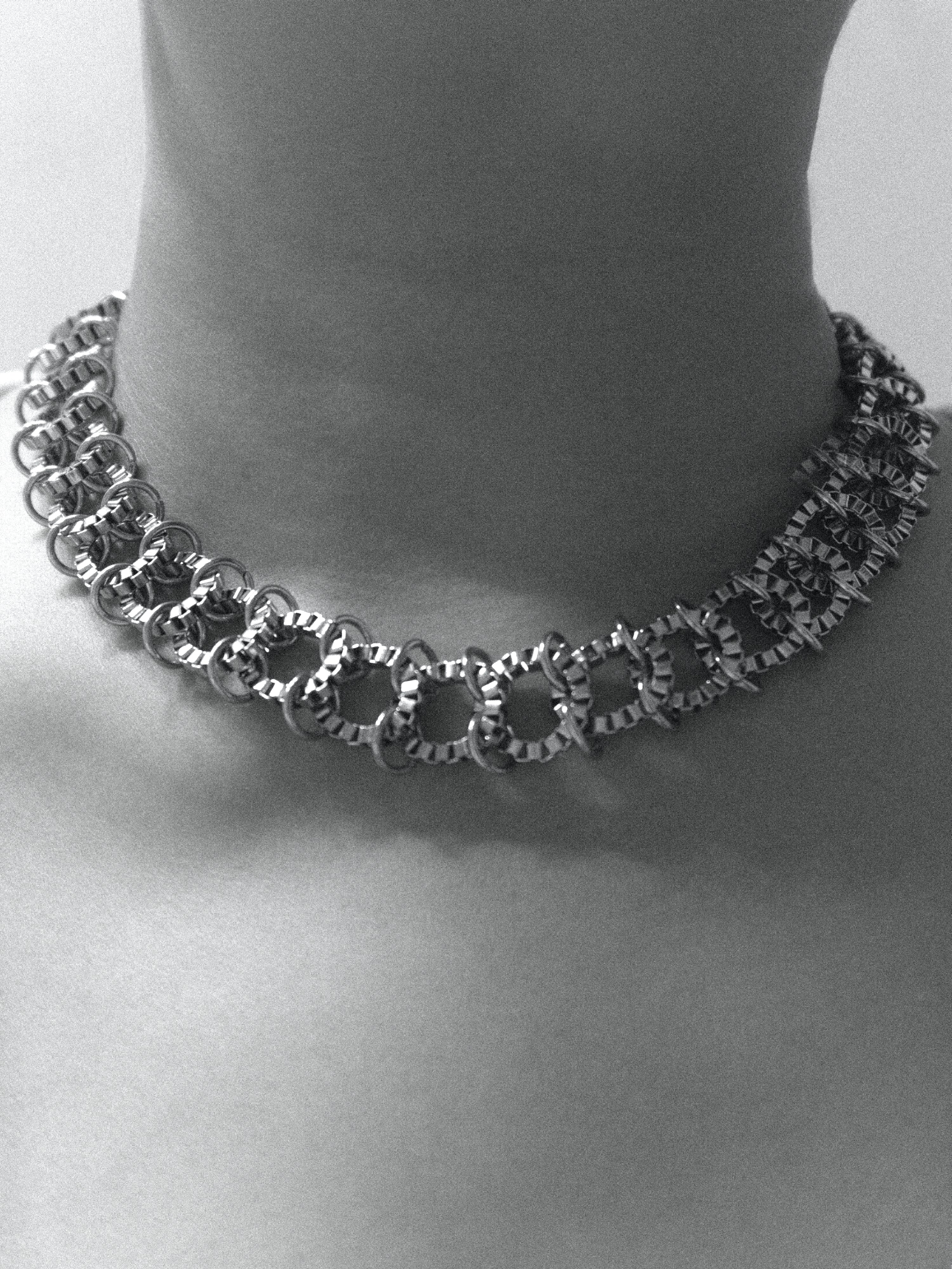 A black and white photograph of a person wearing a silver chain necklace on a plain background