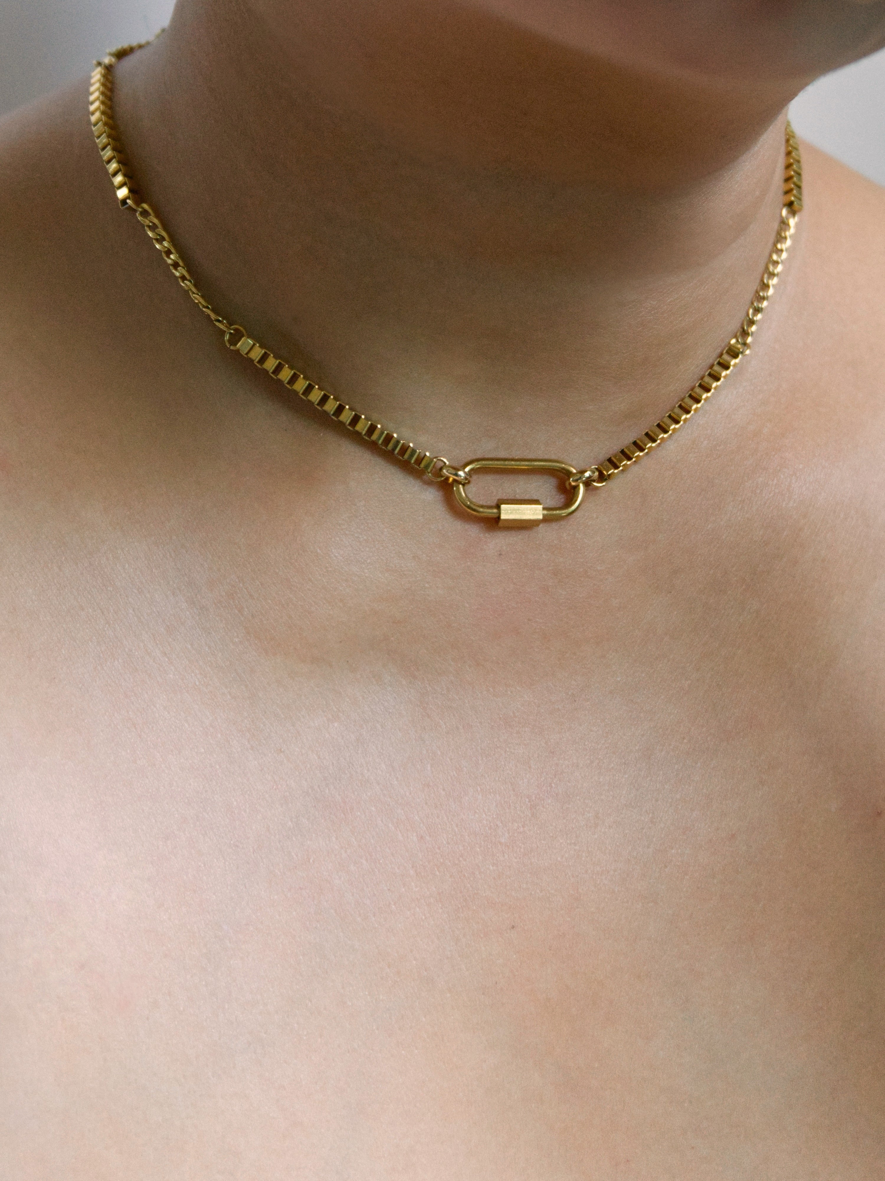 A close-up of a gold chain necklace worn on a person's neck, featuring a polished carabiner link clasp.