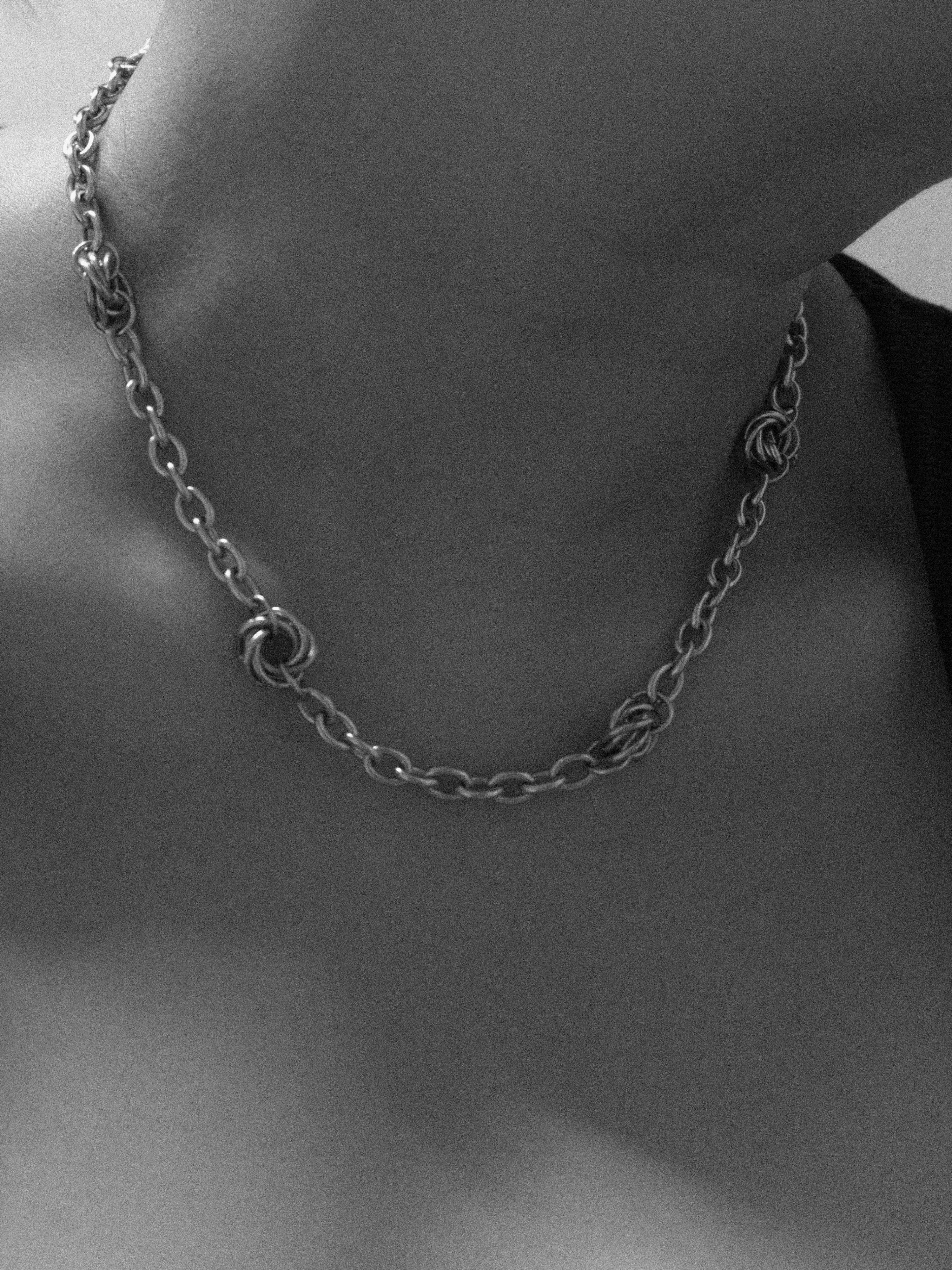 Close-up of a chain necklace on a person in grainy black and white photograph