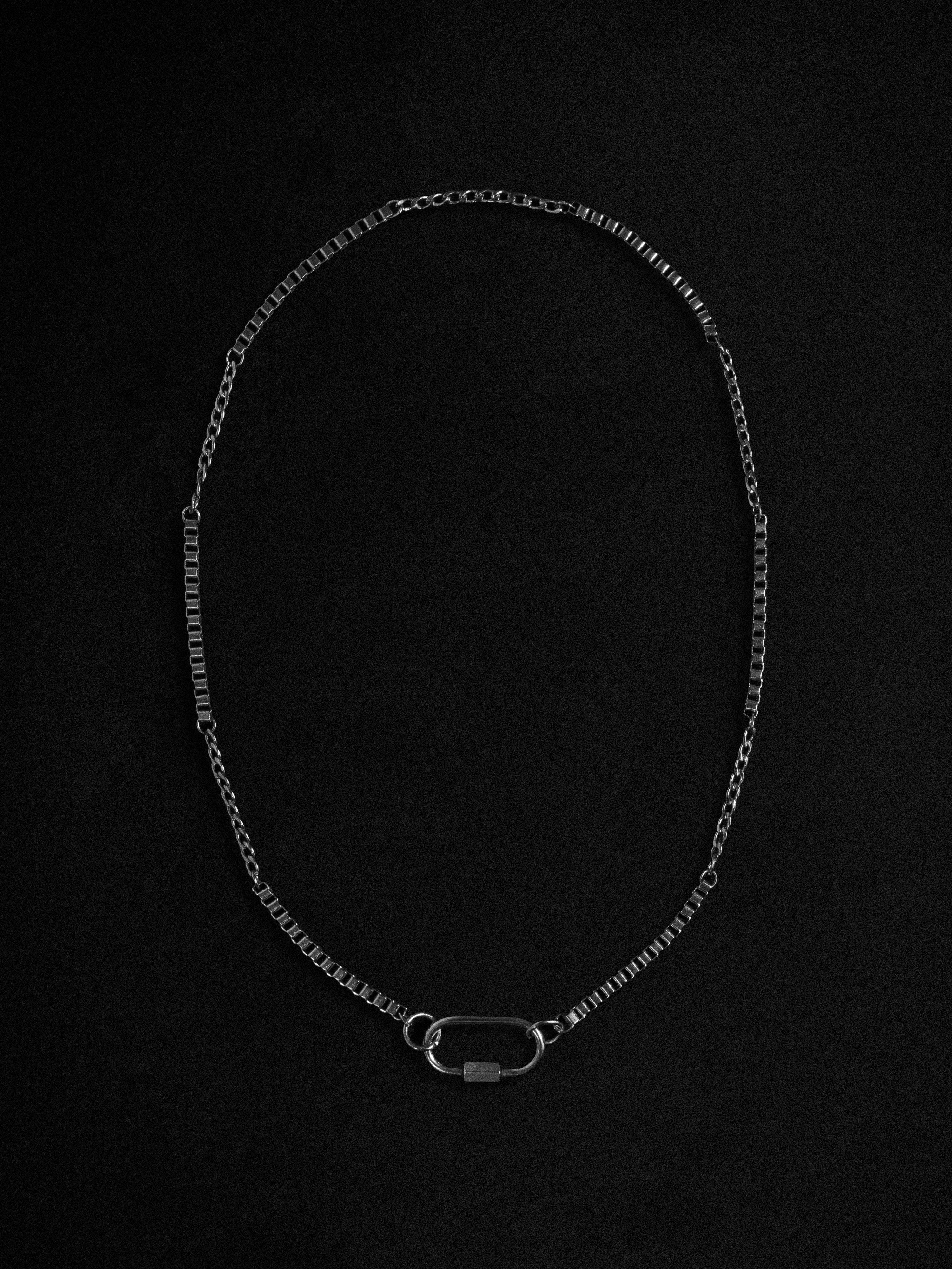 A silver-toned chain necklace with a textured link design and a small oval clasp, displayed on a solid black background.