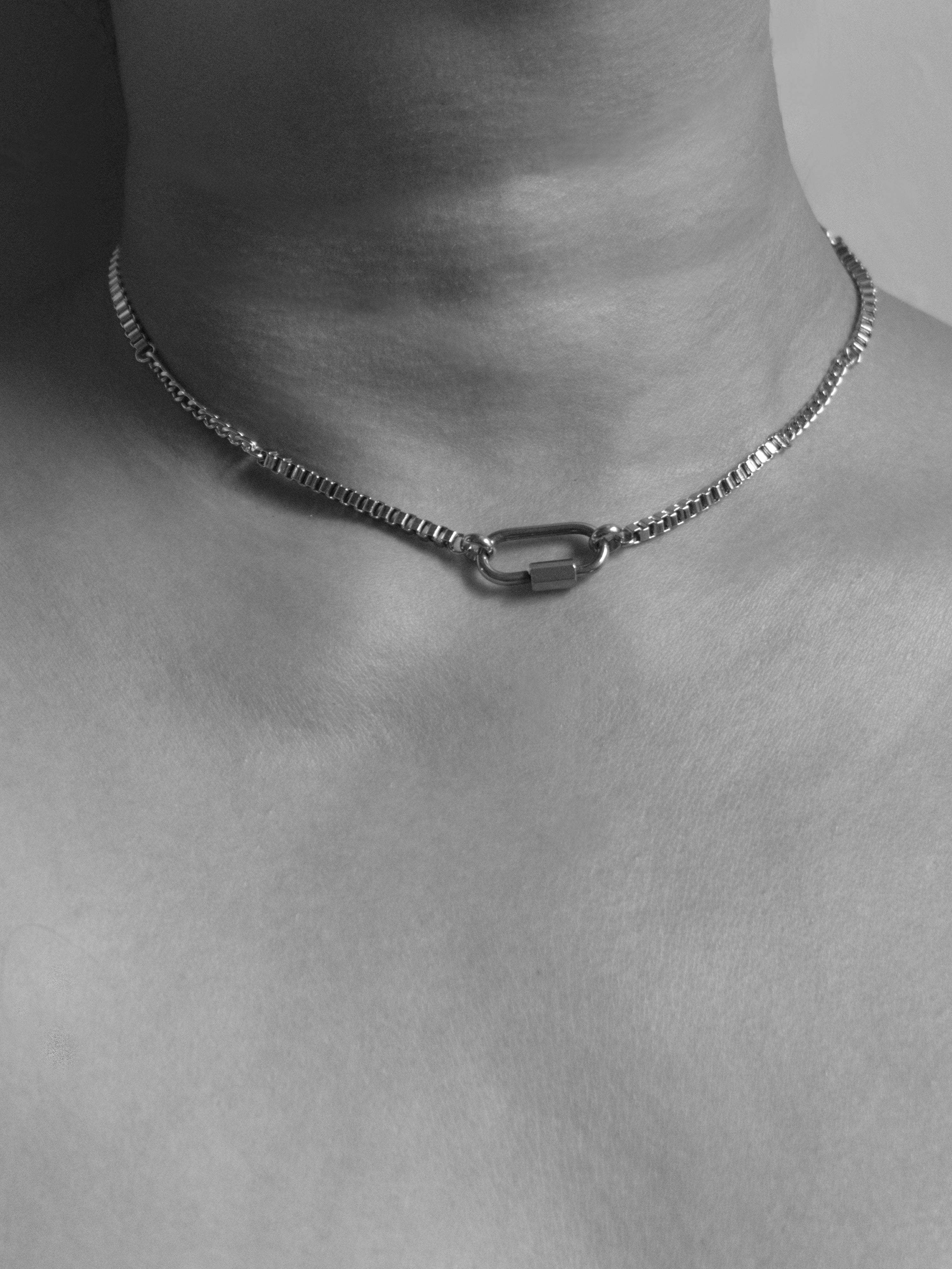 A close-up of a silver chain necklace with a central carabiner-style clasp, worn on a model's neck and upper chest.
