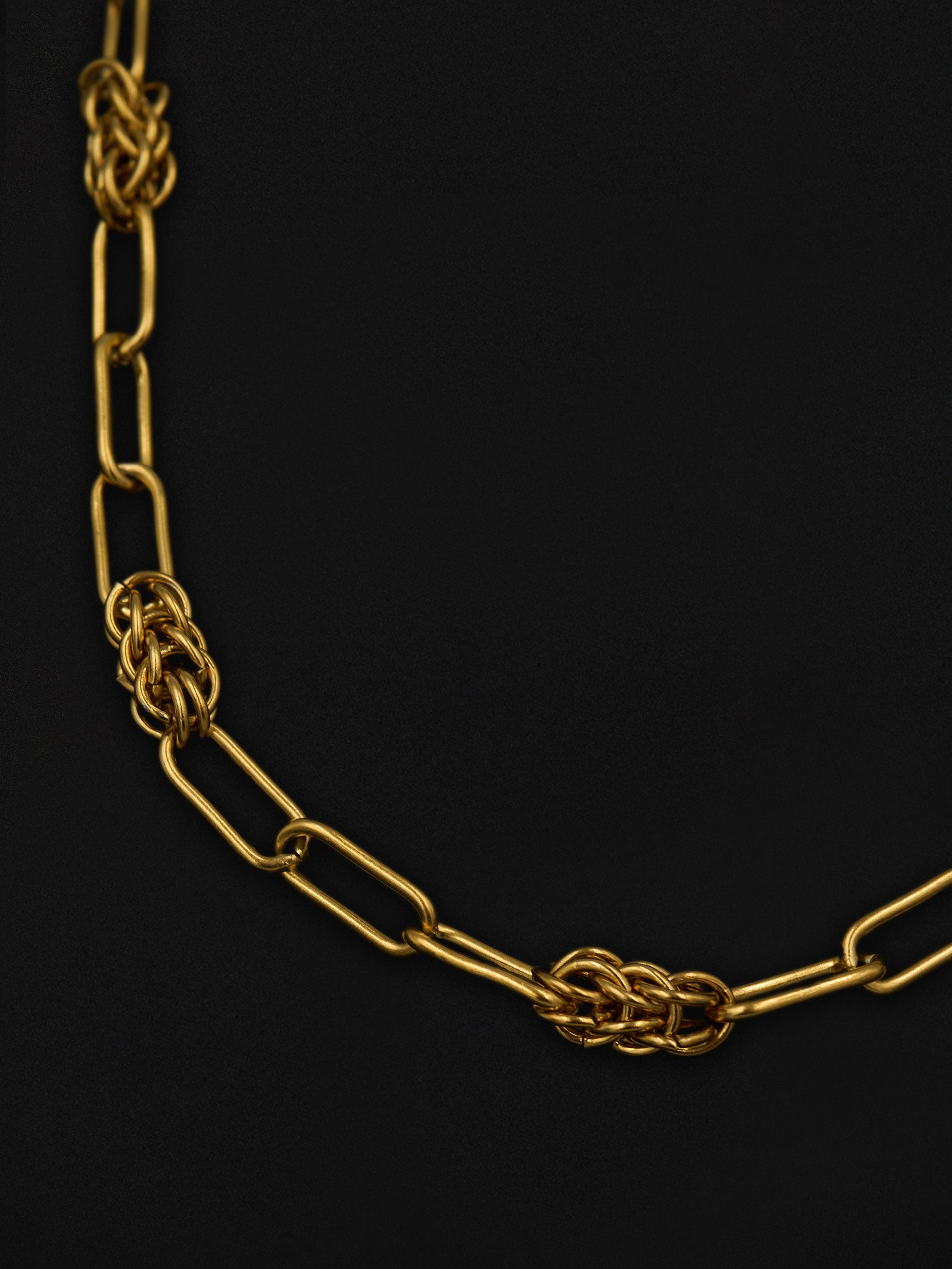Gold chain necklace with a knot design on a black background