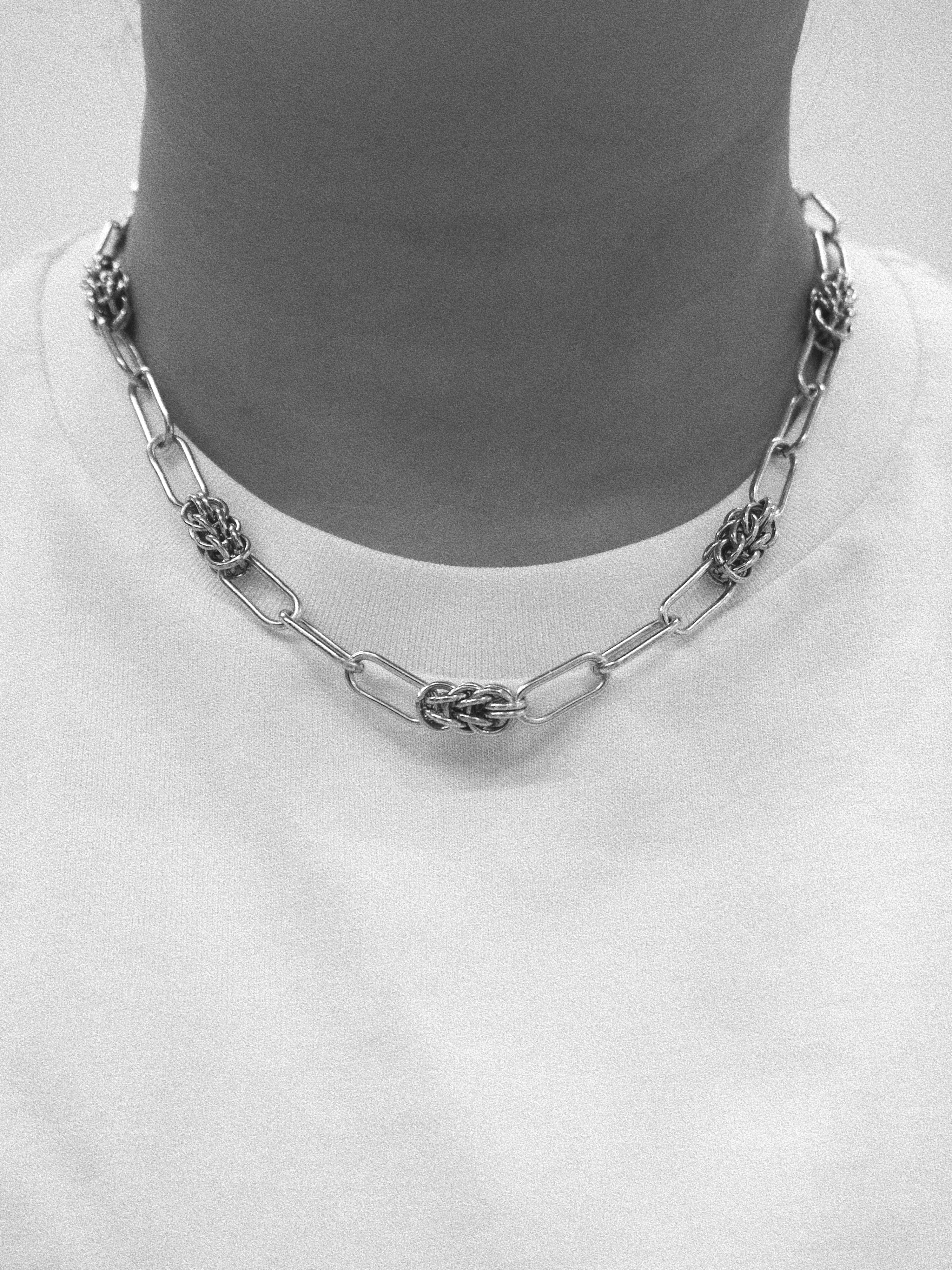 A silver-toned chain necklace with textured, knotted oval links, displayed on a mannequin neck wearing a white t-shirt.