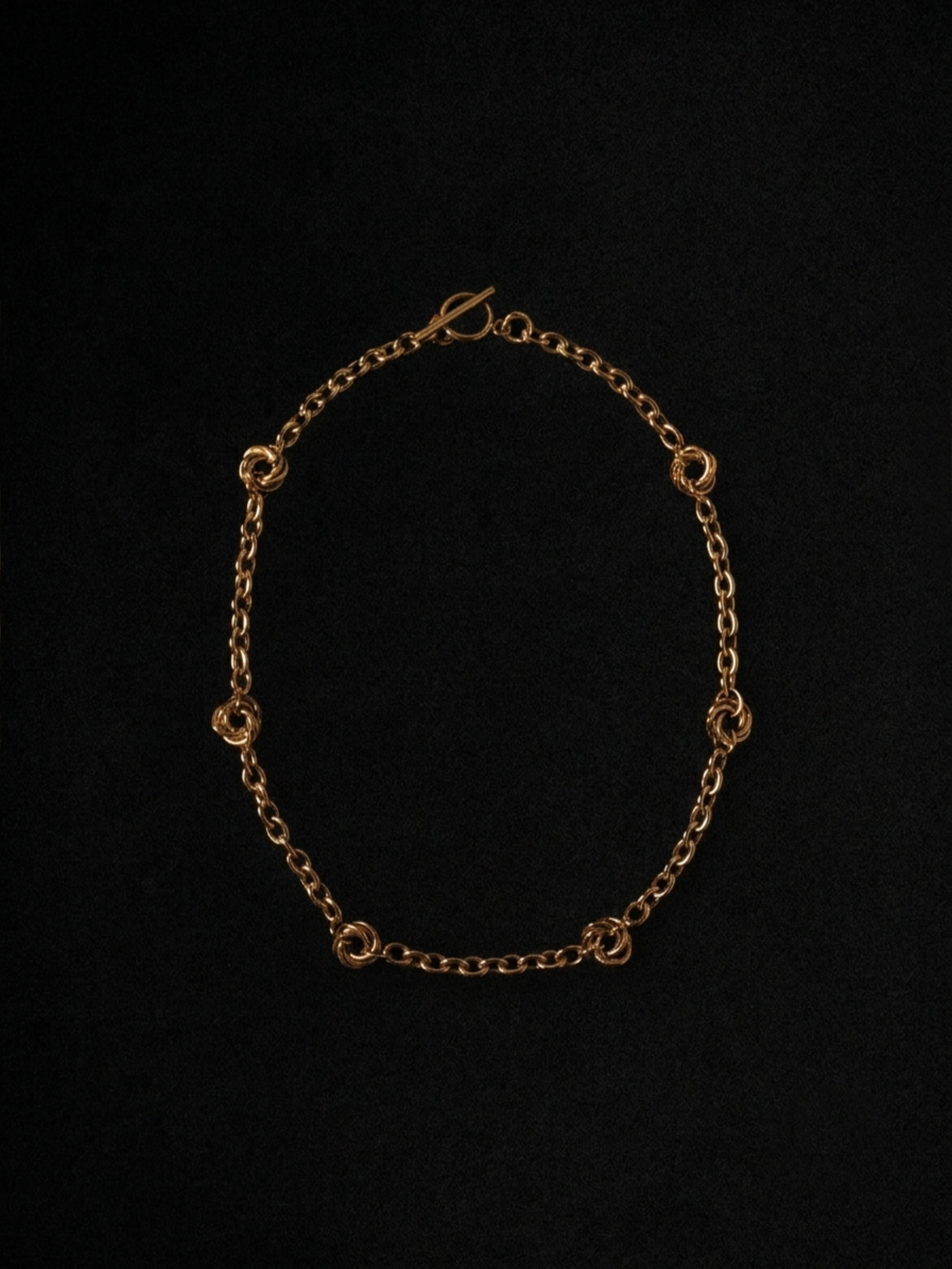 A gold chain necklace with small interlocking circular links, displayed against a solid black background.
