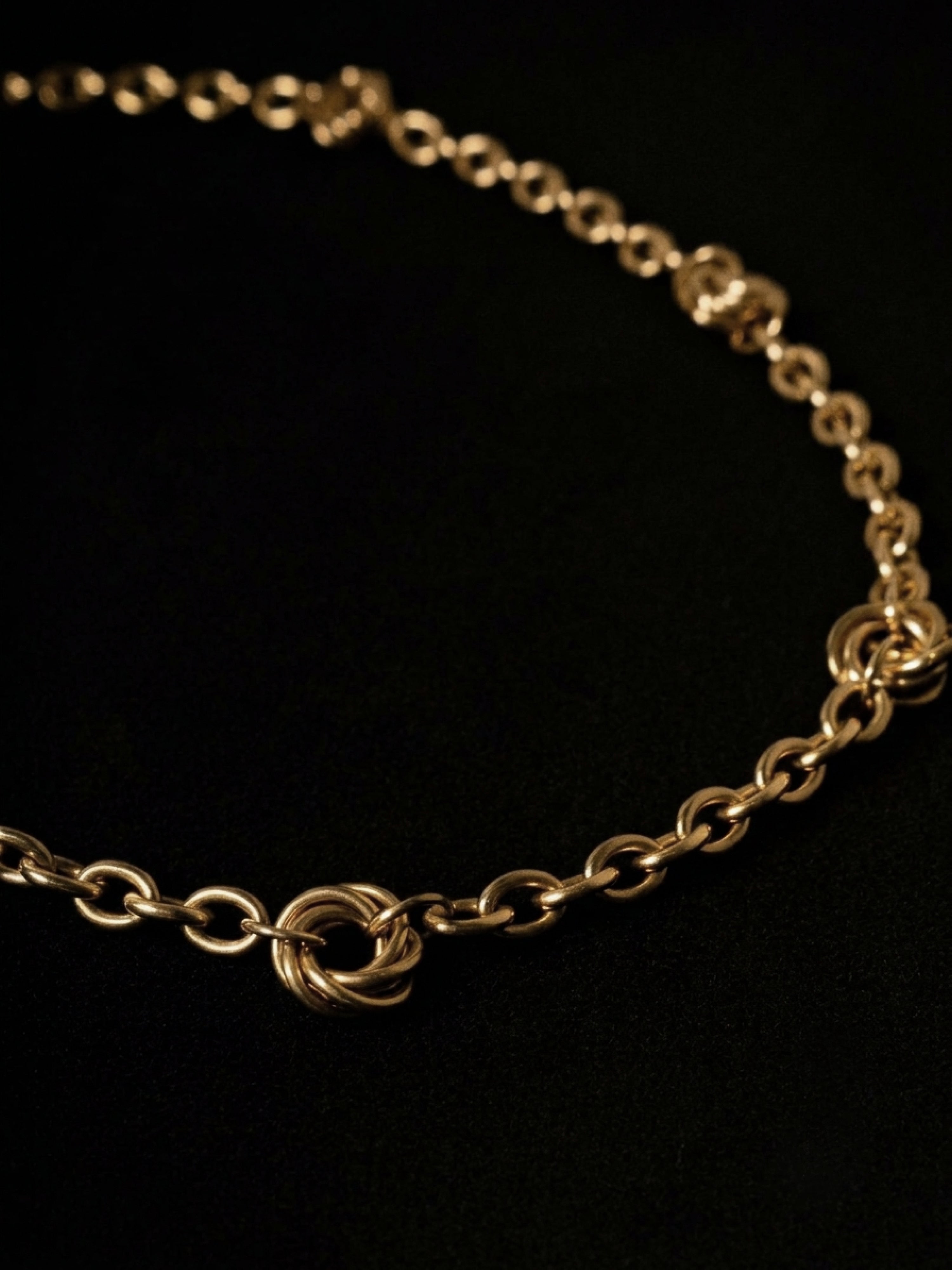 A gold chain necklace with a distinctive twisted ring clasp, displayed on a solid black background.