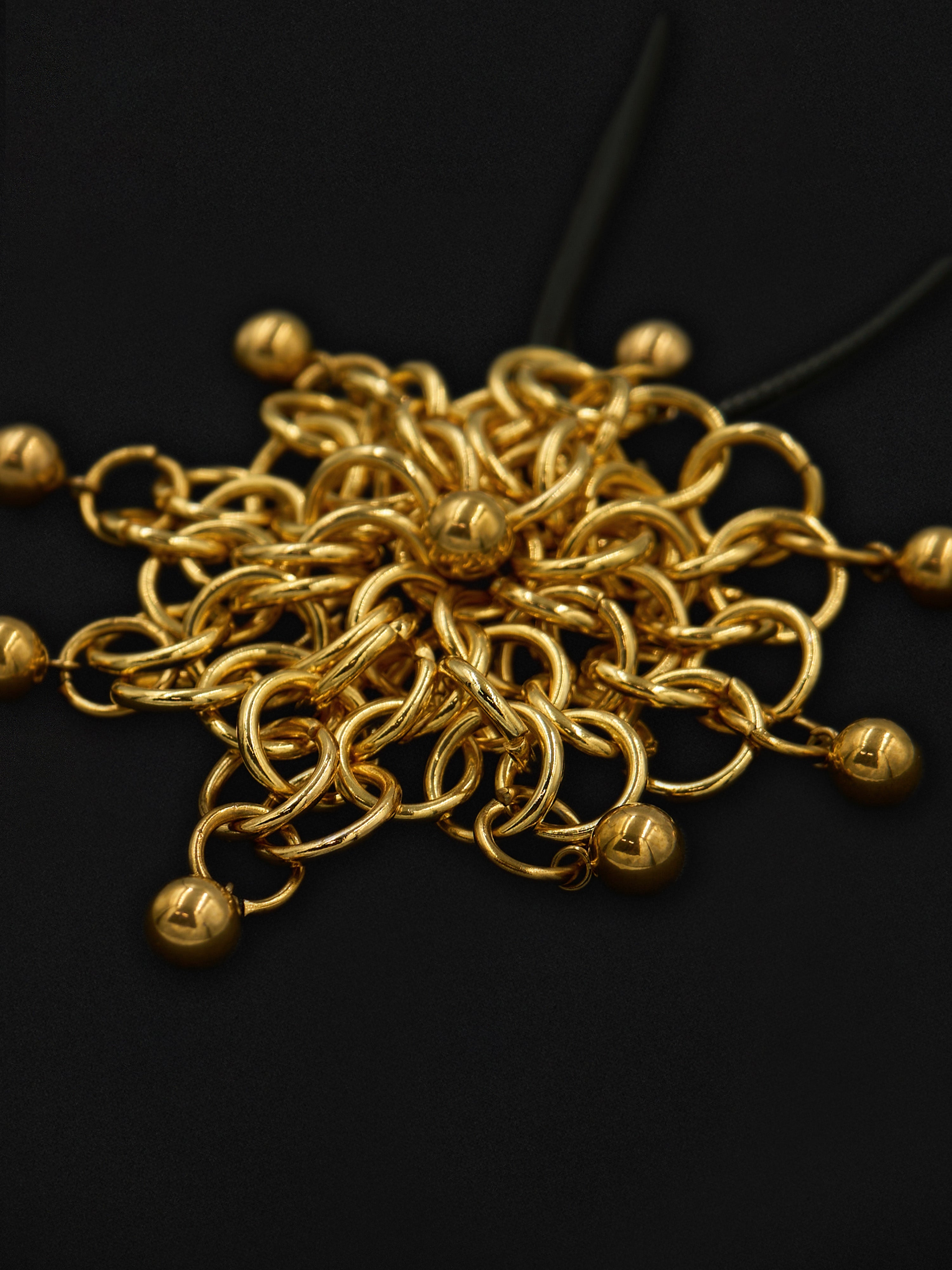 A cluster of gold-colored metal chain links with small spherical beads at the ends, arranged on a dark black background.