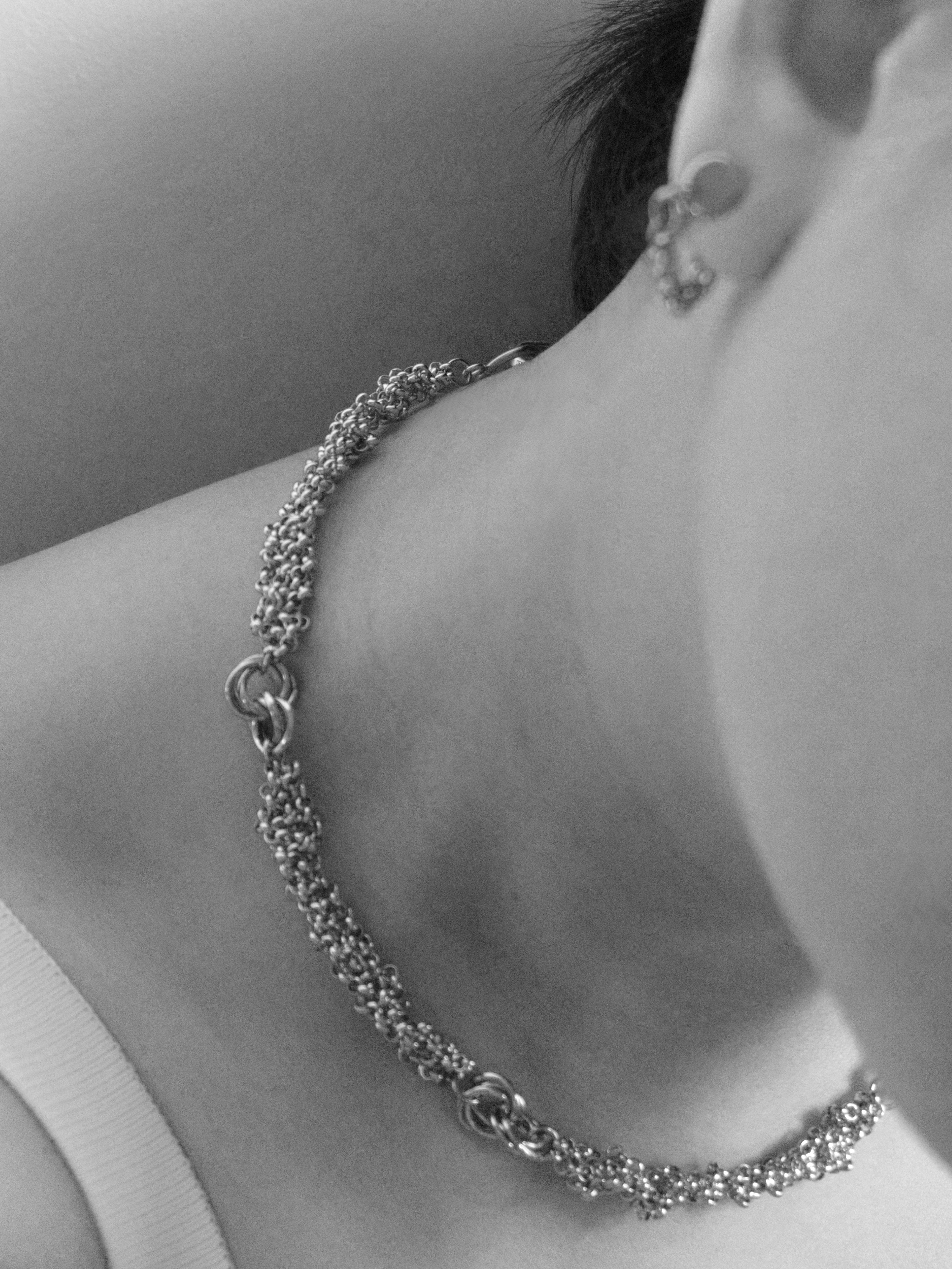 A close-up lifestyle shot of a person wearing a silver chain choker necklace and matching silver stud earrings.