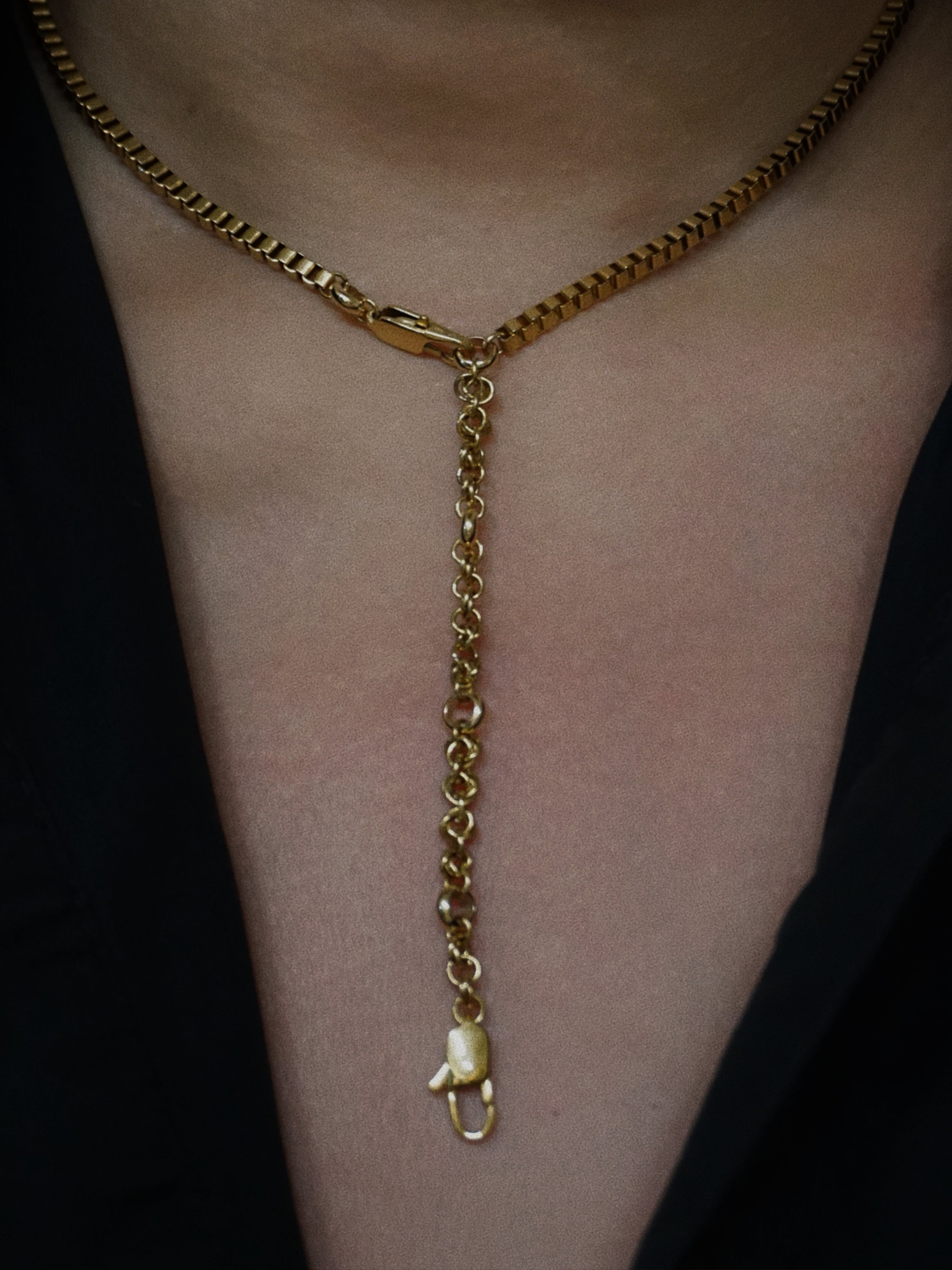 Gold chain necklace with a pendant on a person's neck wearing a black shirt 