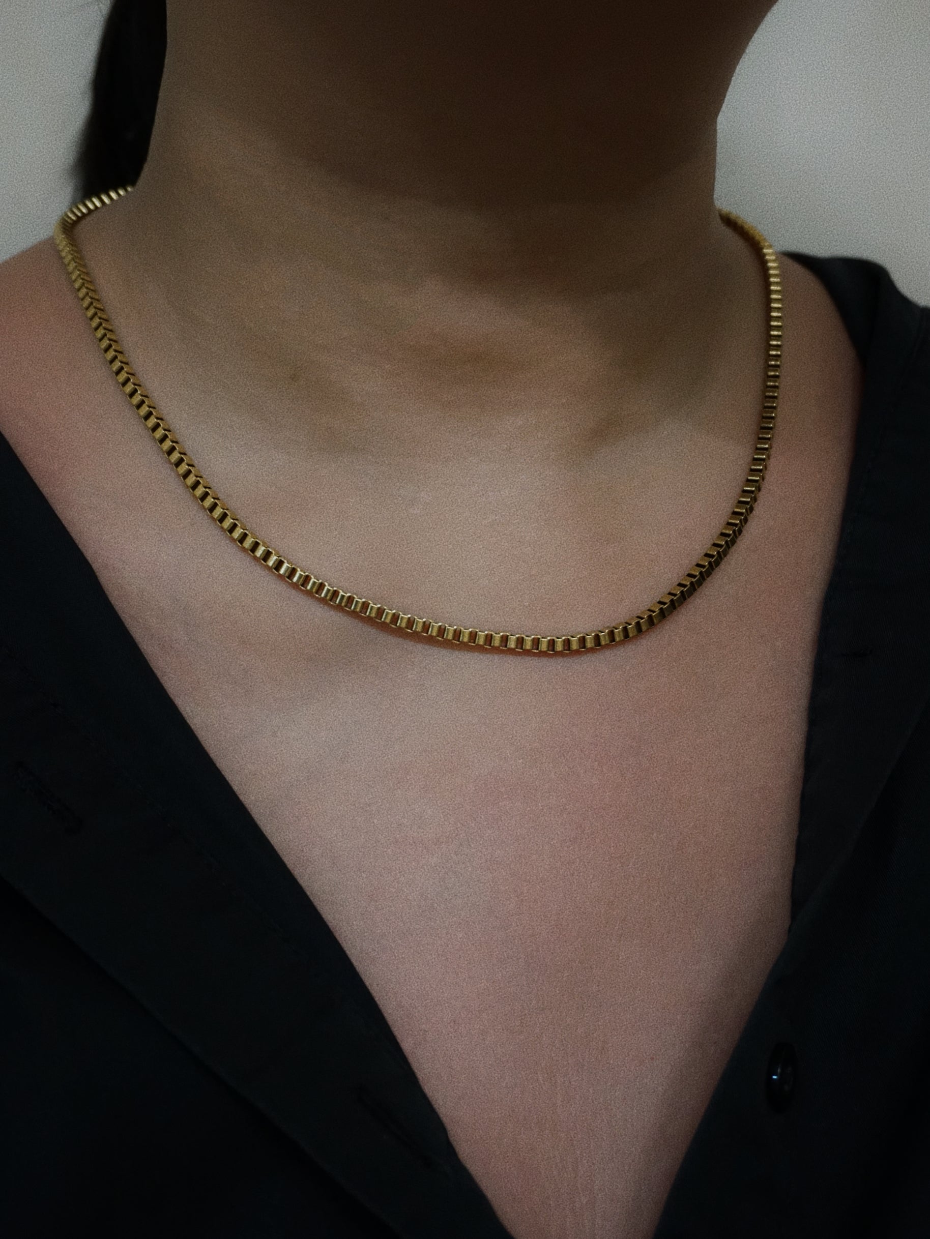 Gold chain necklace on a person wearing a black top.