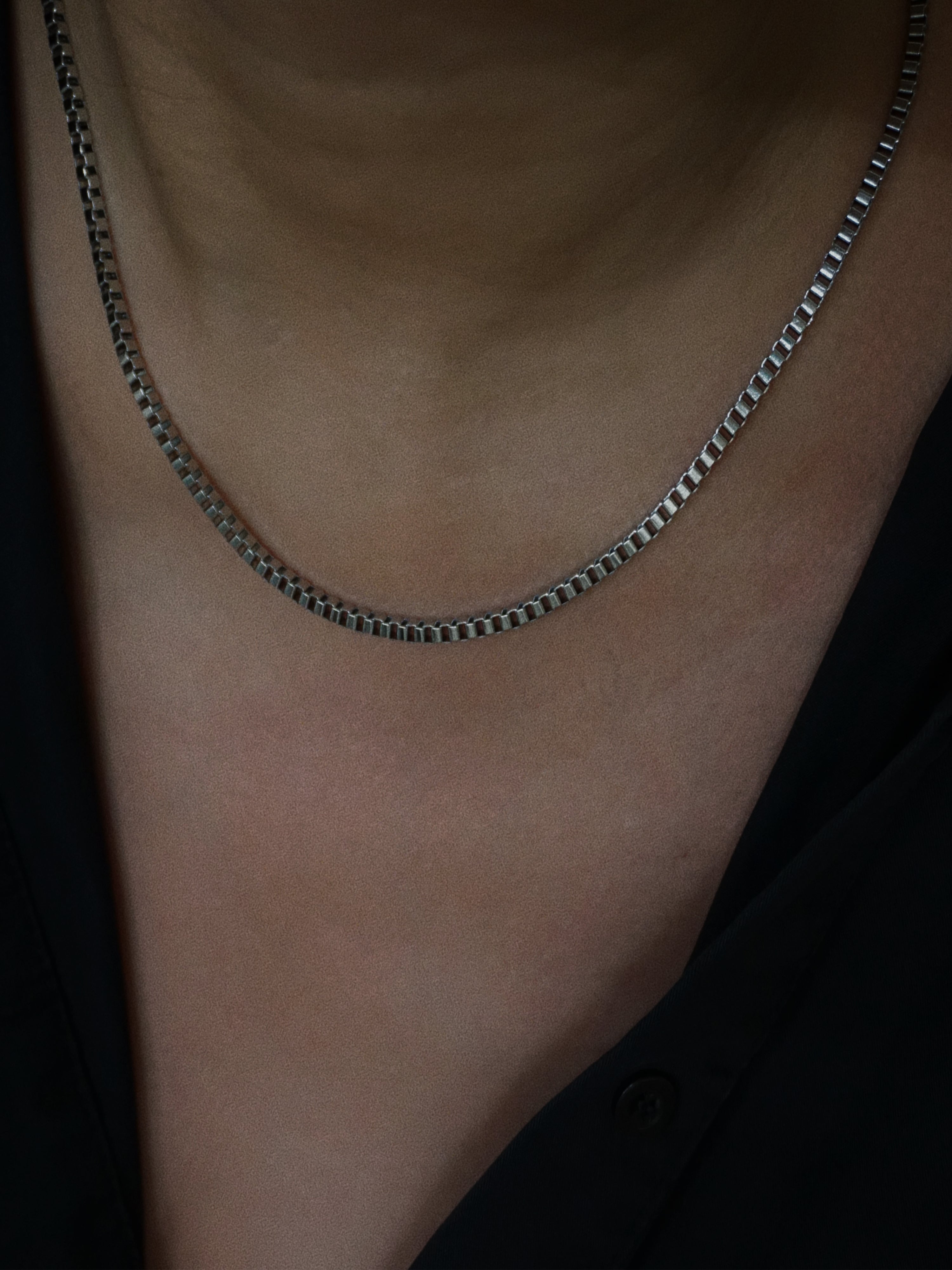 Silver chain necklace on a person's neck with a dark background