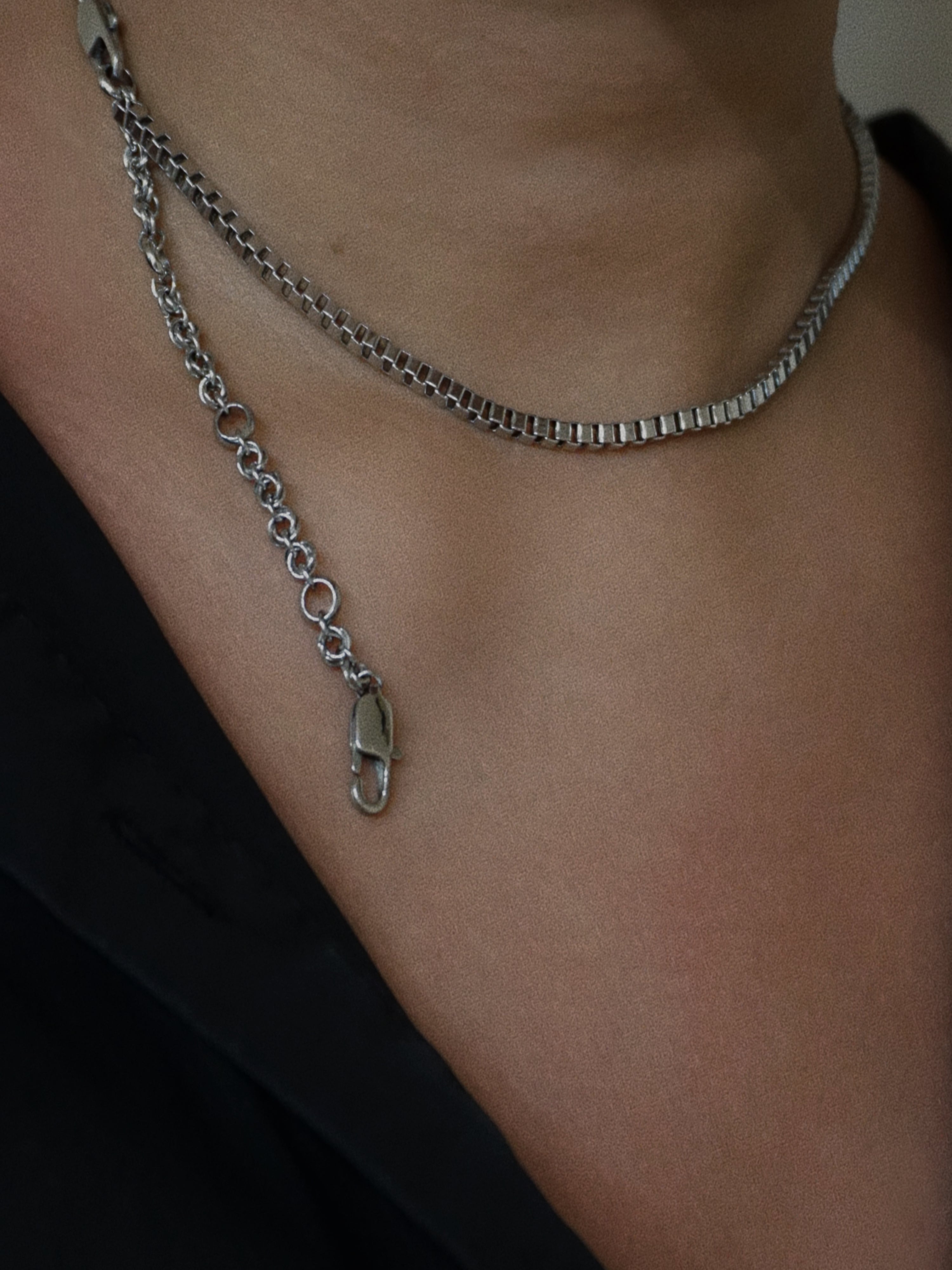 Silver chain necklace on a person's neck wearing a black top