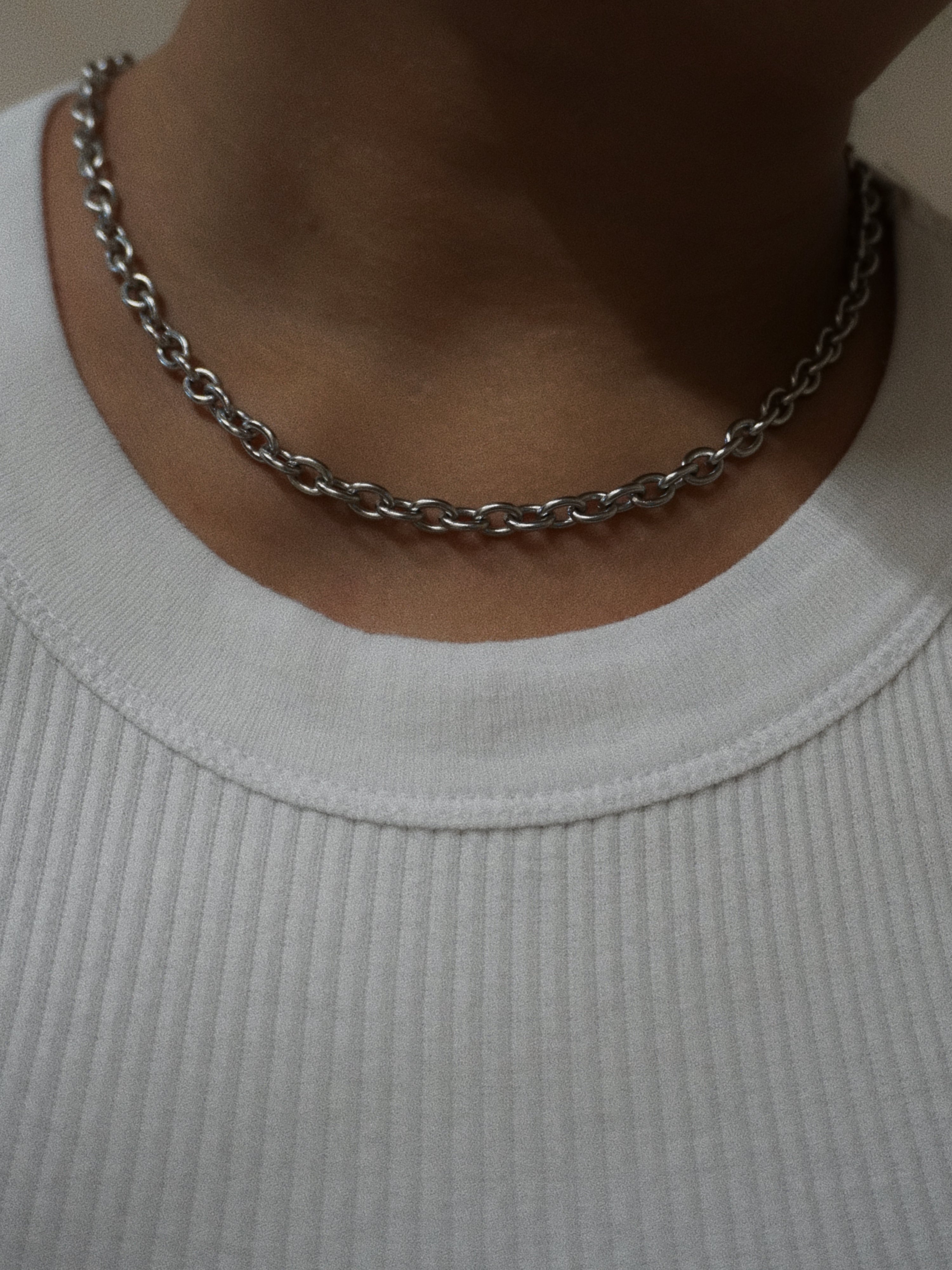 Silver chain necklace worn by a person on a plain background