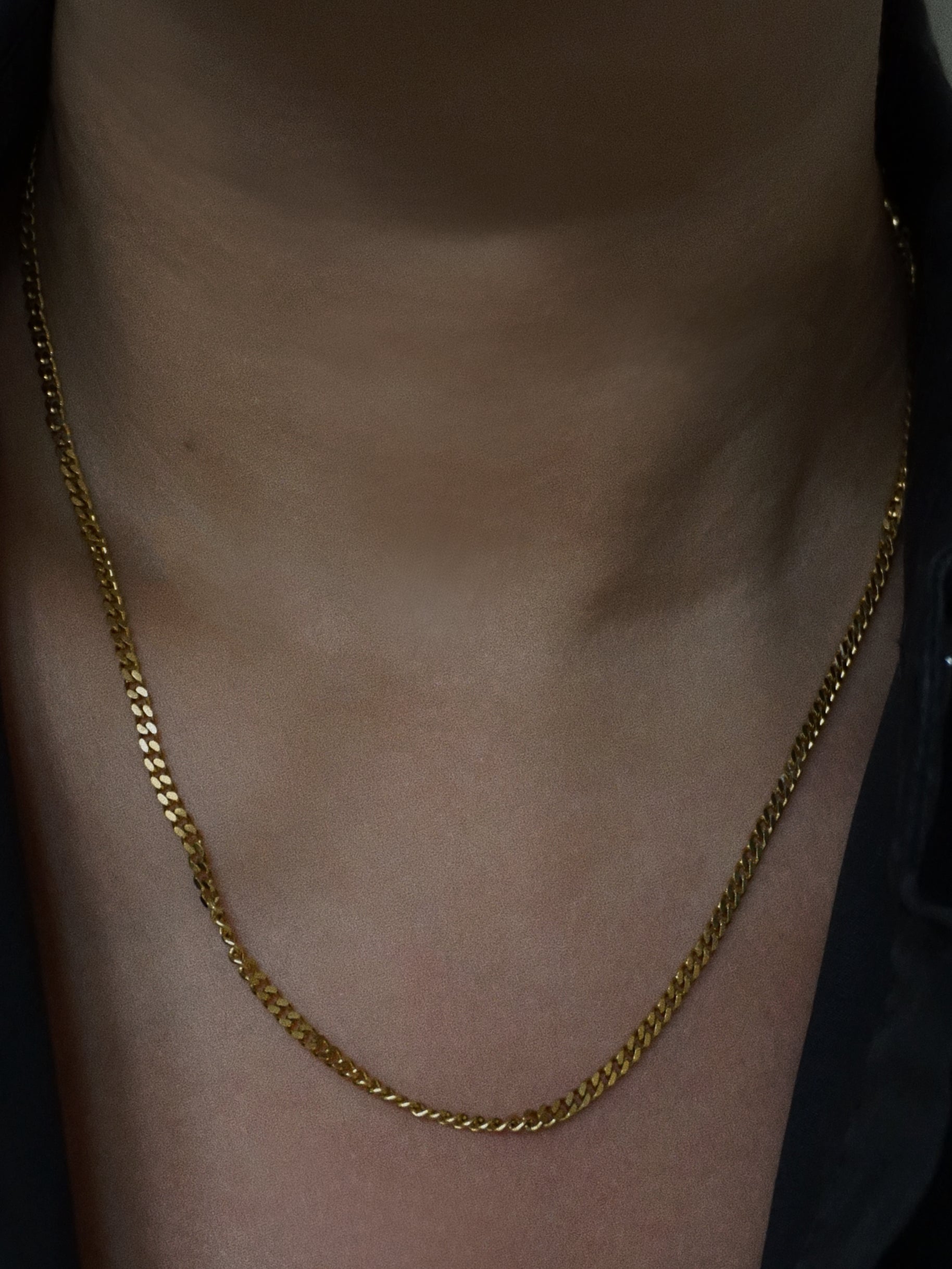 Gold chain necklace on a person's neck with a dark background