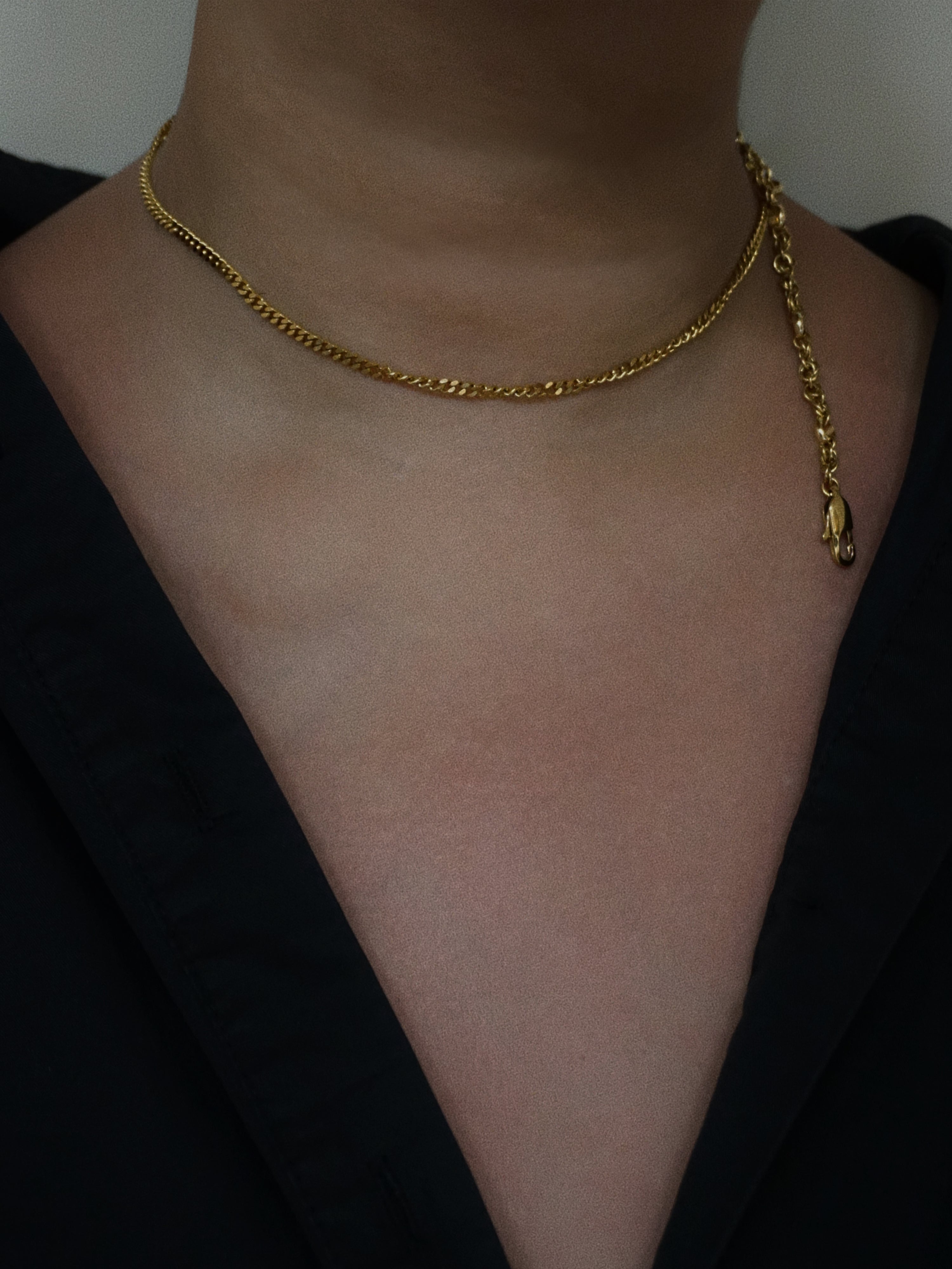 Gold chain necklace on a person wearing a black top against a neutral background