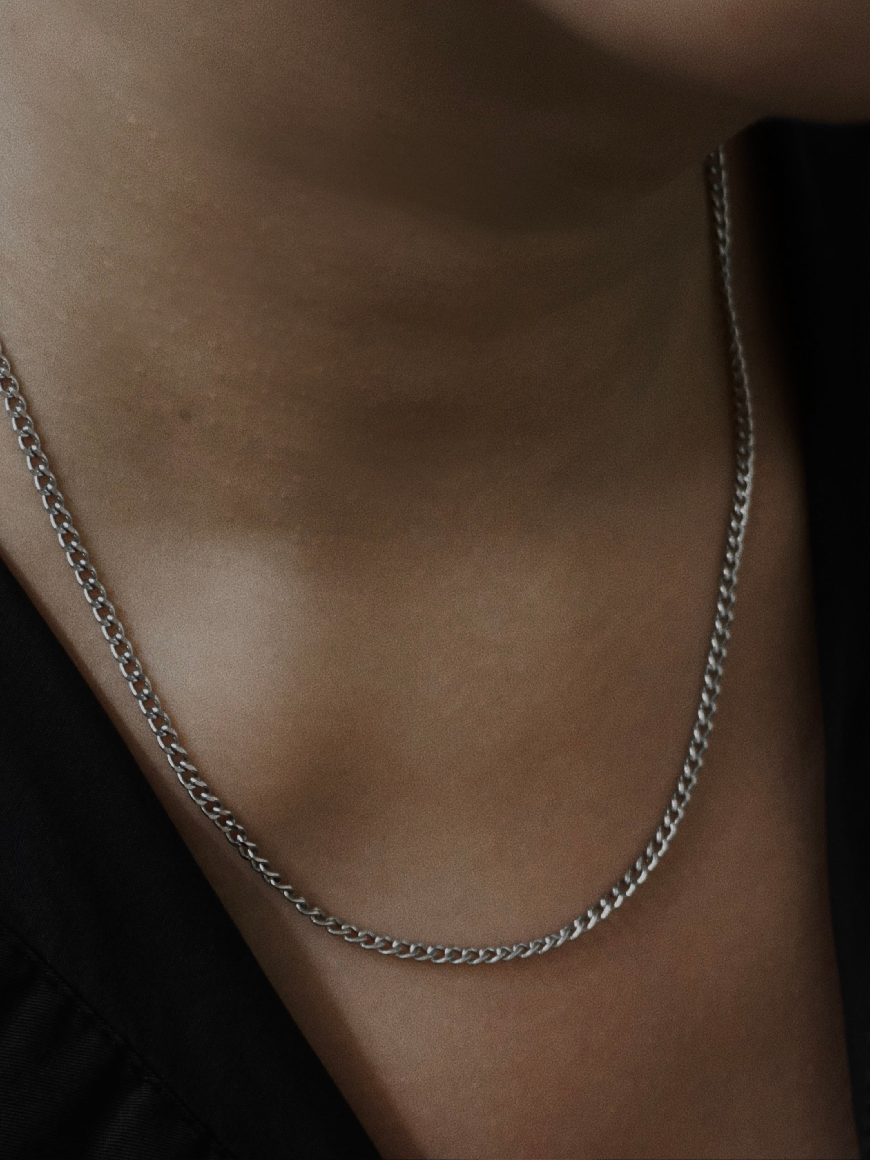 Silver chain necklace on a person's neck against a dark background