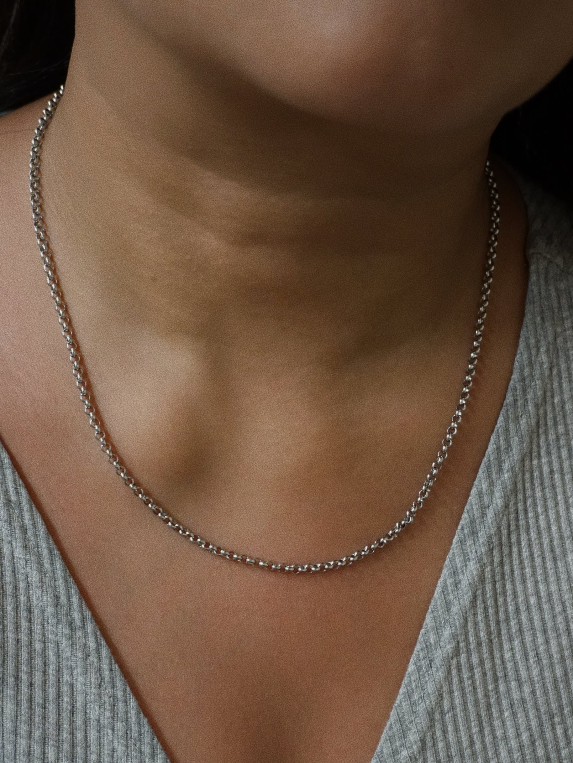 Silver chain necklace worn by a person with a neutral background