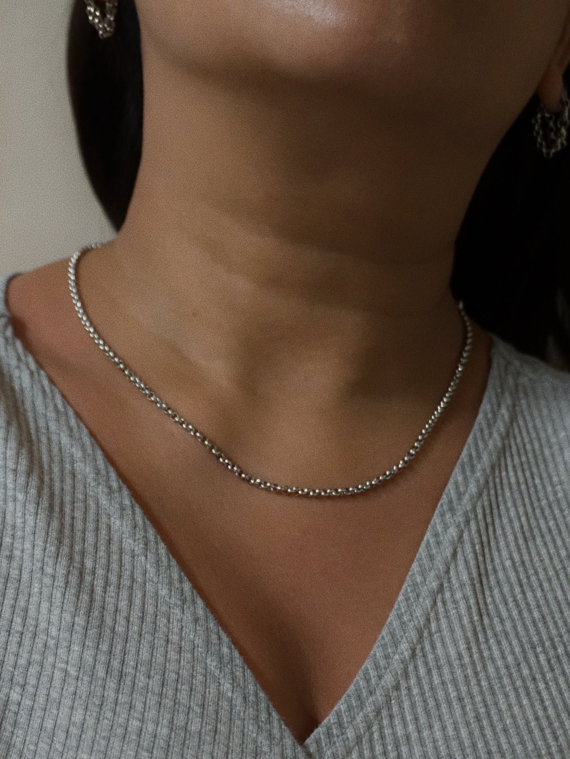 Close-up of a person wearing a silver necklace with a neutral background