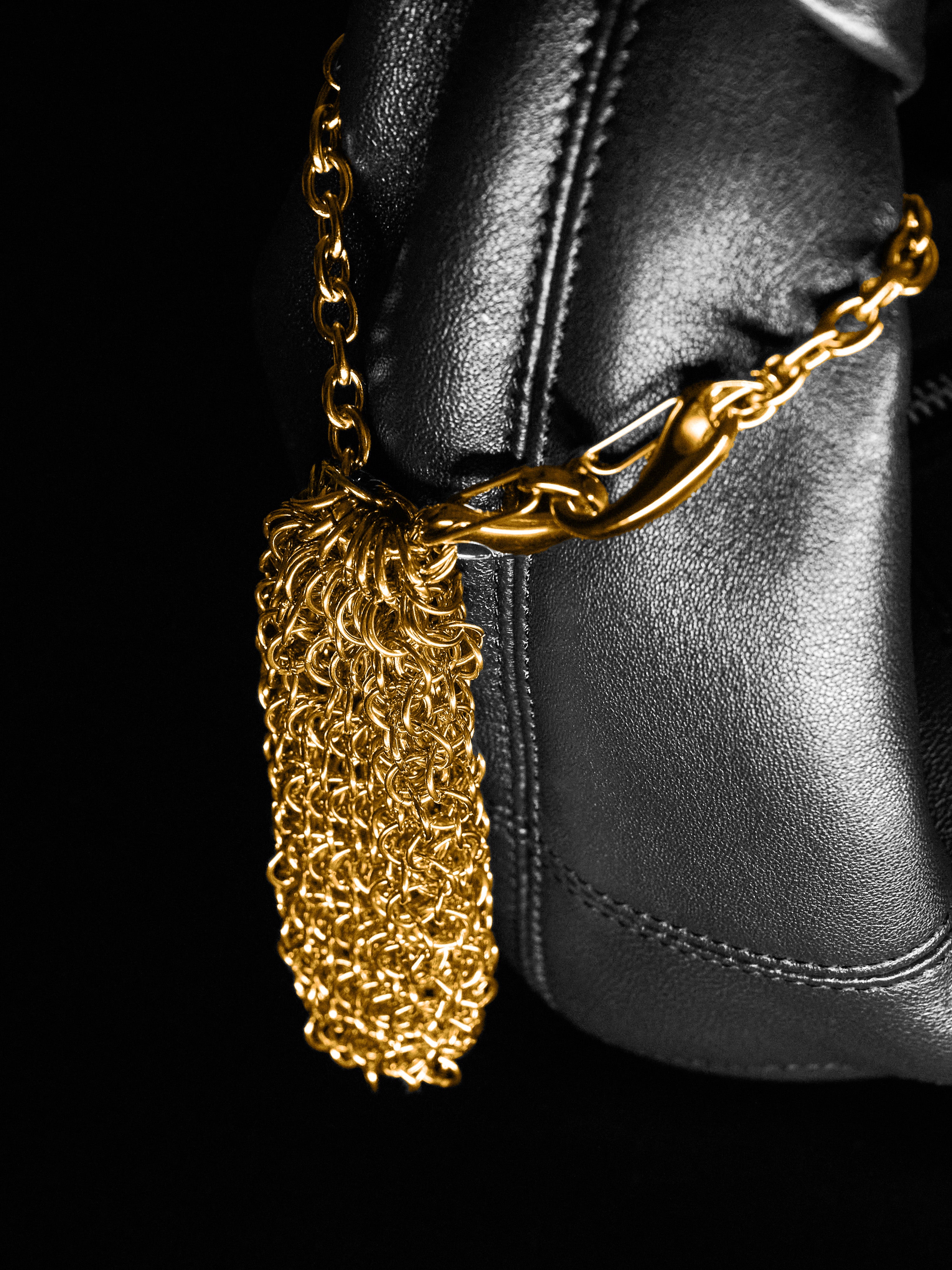 Gold chainmaille pouch hanging on a leather bag on a black background 