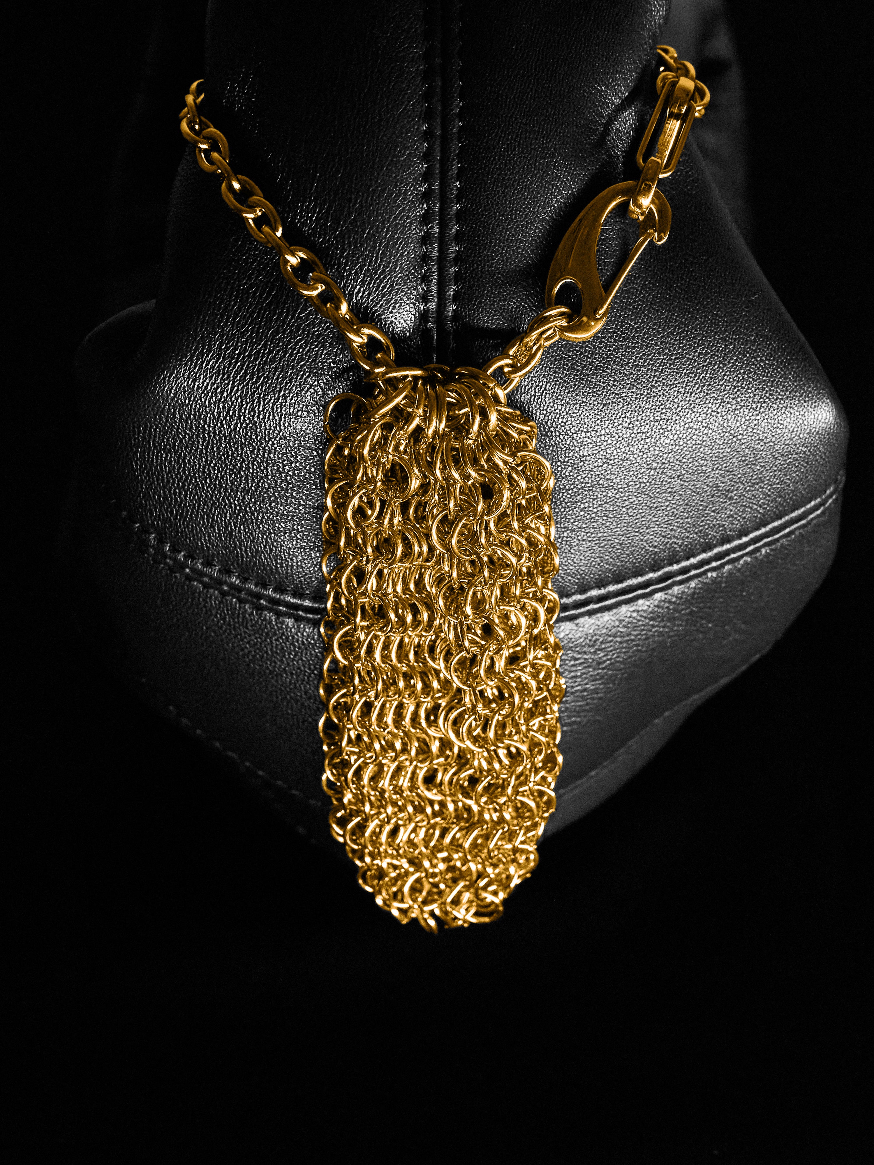 Gold chainmaille pouch hanging on the side of the leather bag on a black background 
