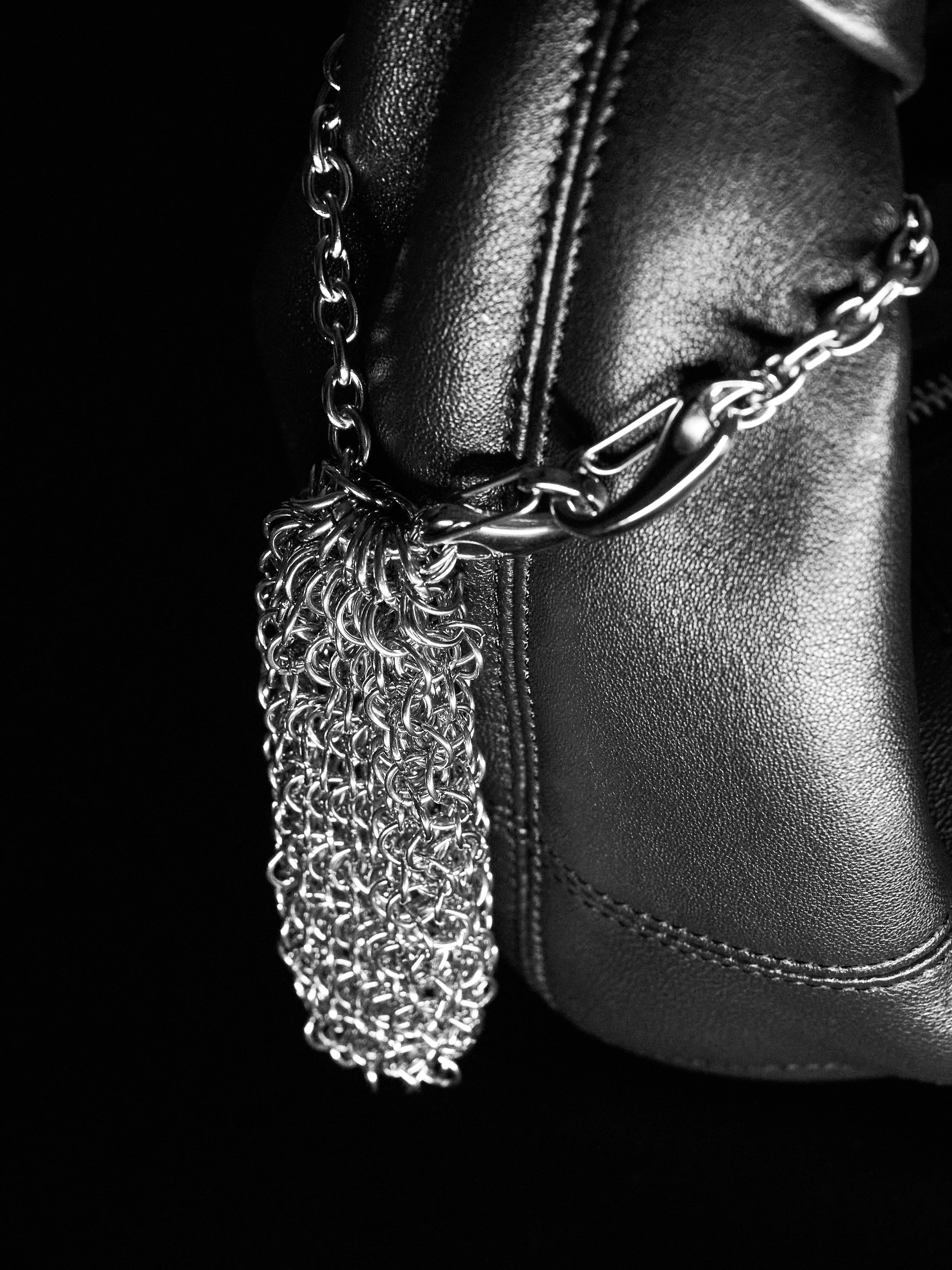 Silver chainmaille pouch hanging on a leather bag against a black background 