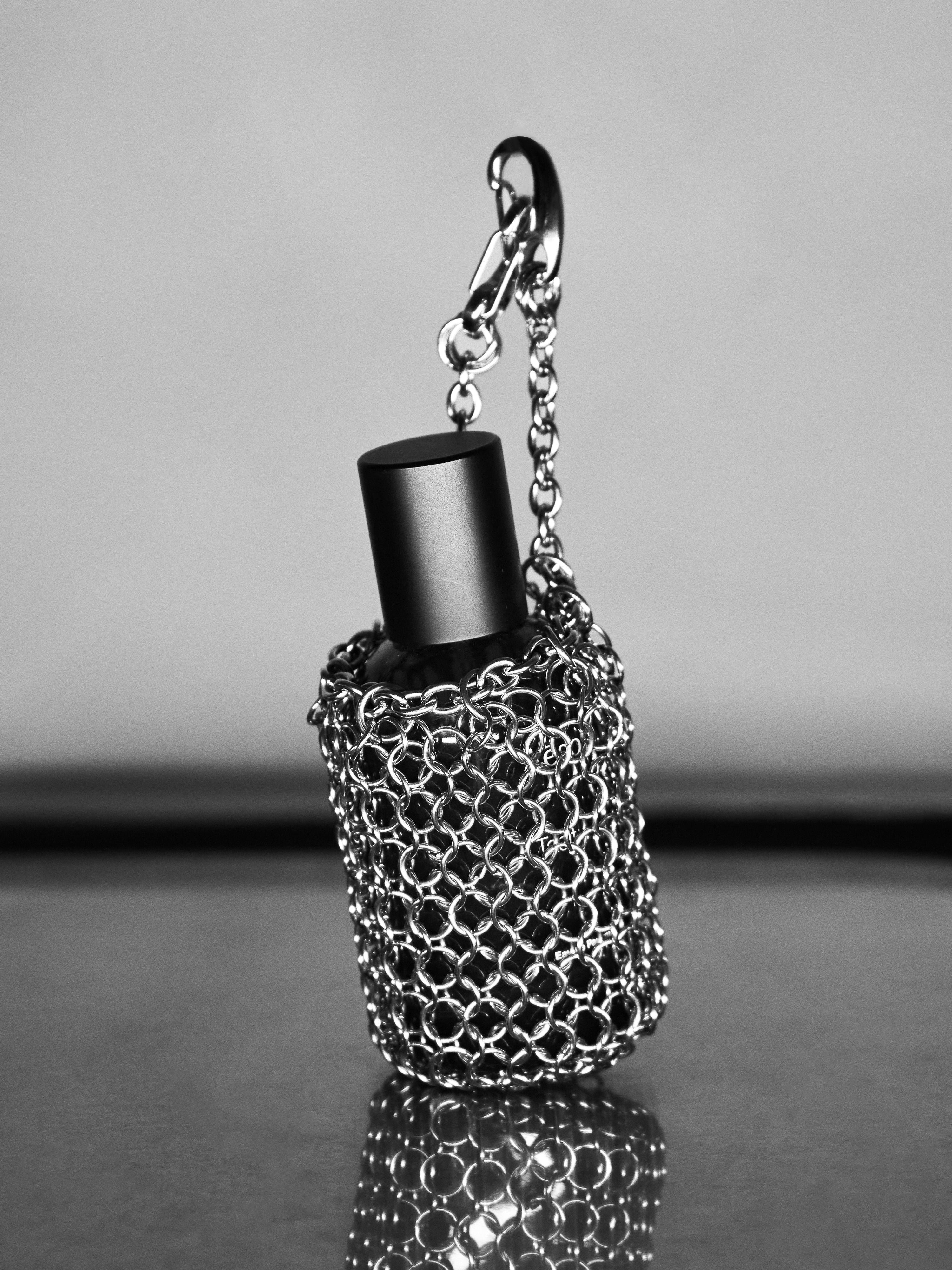 Black perfume bottle with unique chainmaille pouch holding it on a reflective surface